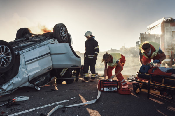 On the Car Crash Traffic Accident: Paramedics and Firefighters Rescue Injured Trapped Victims. Medics give First Aid to Female on Stretchers. Firemen Use Hydraulic Cutters Spreader to Open Vehicle