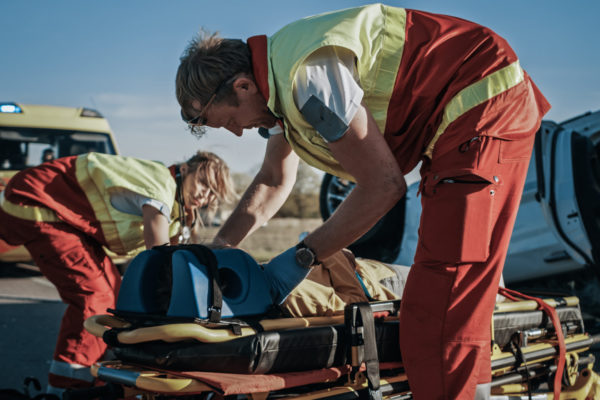 On the Car Crash Traffic Accident Scene: Paramedics and Firefighters Rescue Injured Victim Trapped in the Vehicle. Extricate Person Using Stretchers, Give First Aid and Transport Them to Hospital